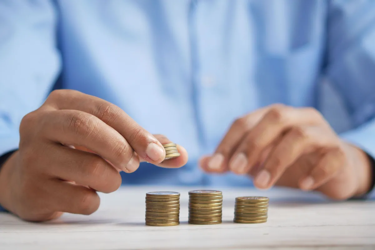 Unas manos reparten monedas en tres pilas separadas sobre una mesa, en lugar de acumularlas en un solo montón.